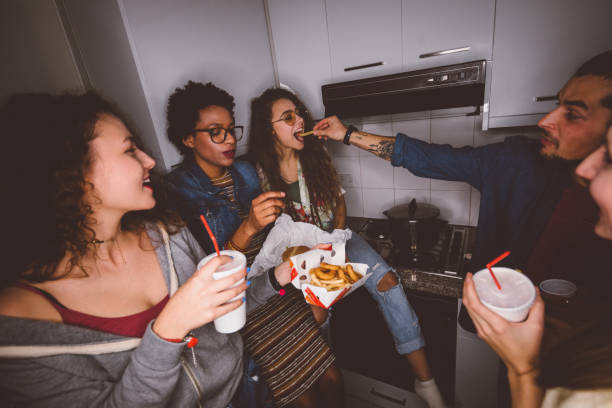 Young multi-ethnic hipster friends having fun at college dorm party and eating fast food